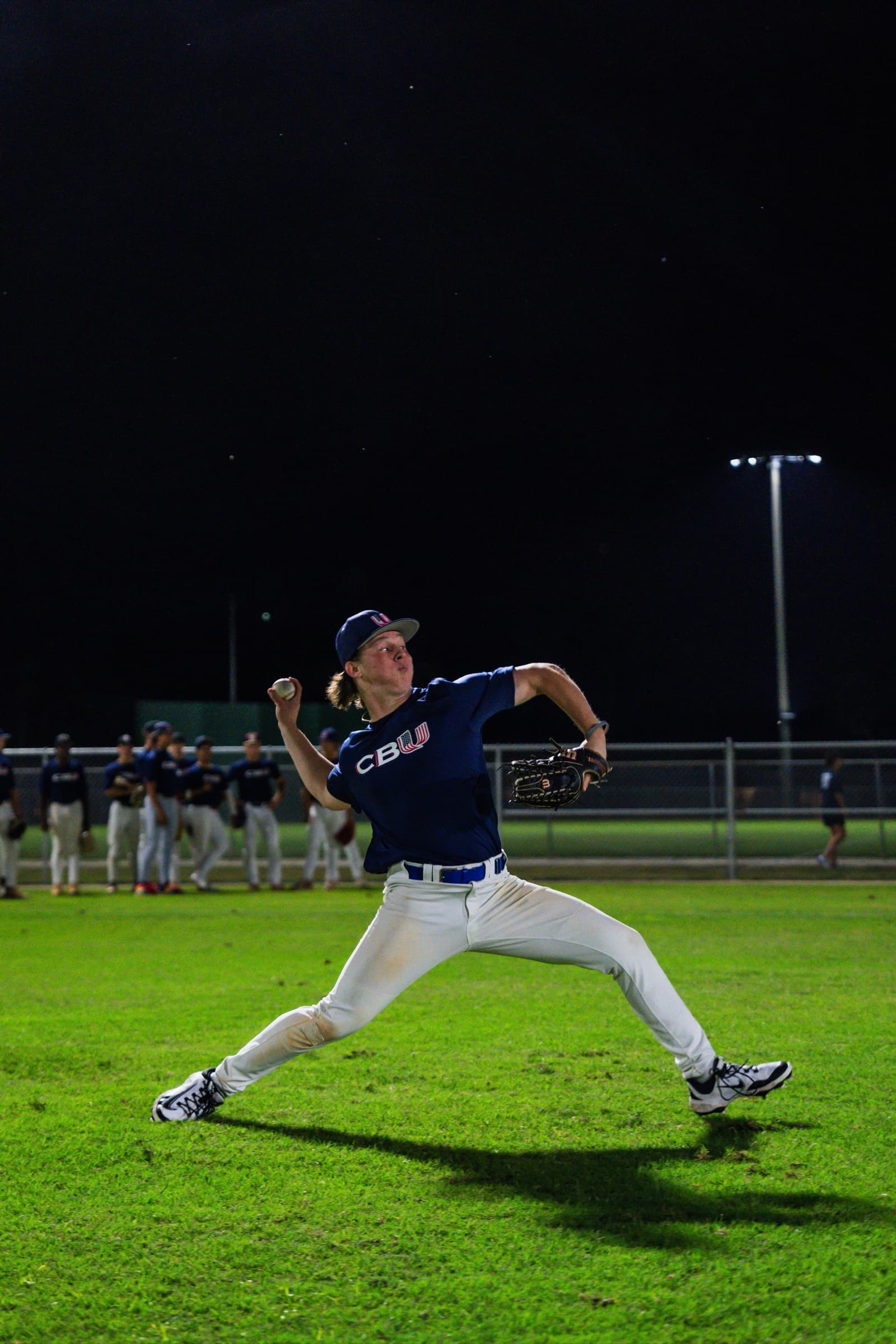 High school player in full pitching motion under stadium lights